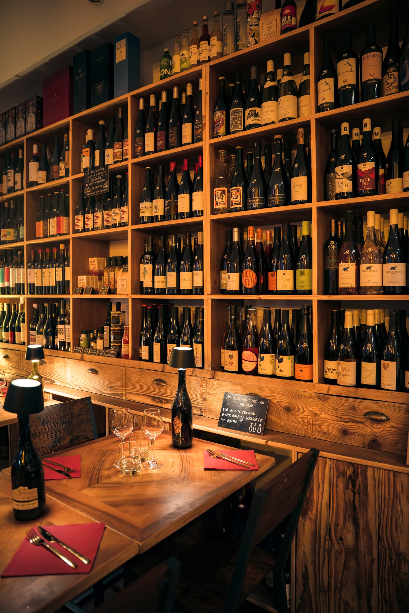 La cave à vins naturels du Bistrot du Fromager le soir, table dressée devant le mur de bouteilles